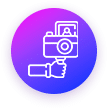 Icon of a hand holding a camera on a vibrant gradient background of purple and blue. The design is simple and outlined in white, set within a dark purple circular border.