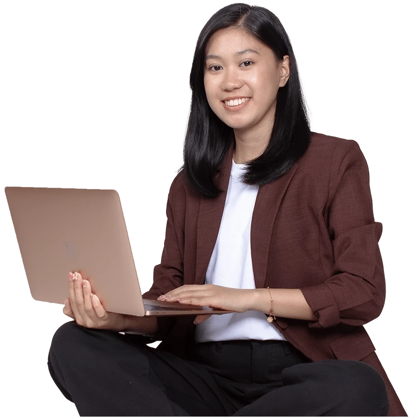 A person with long black hair, wearing a maroon blazer and white shirt, sits cross-legged with a laptop on their lap, smiling at the camera. This content creator exudes confidence against the plain background.