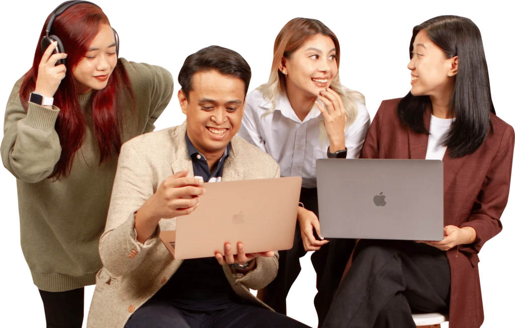 A group of four people are gathered together, smiling and talking. Two are holding laptops, and one is wearing headphones. Theyre dressed in casual and business attire, appearing engaged in a discussion.
