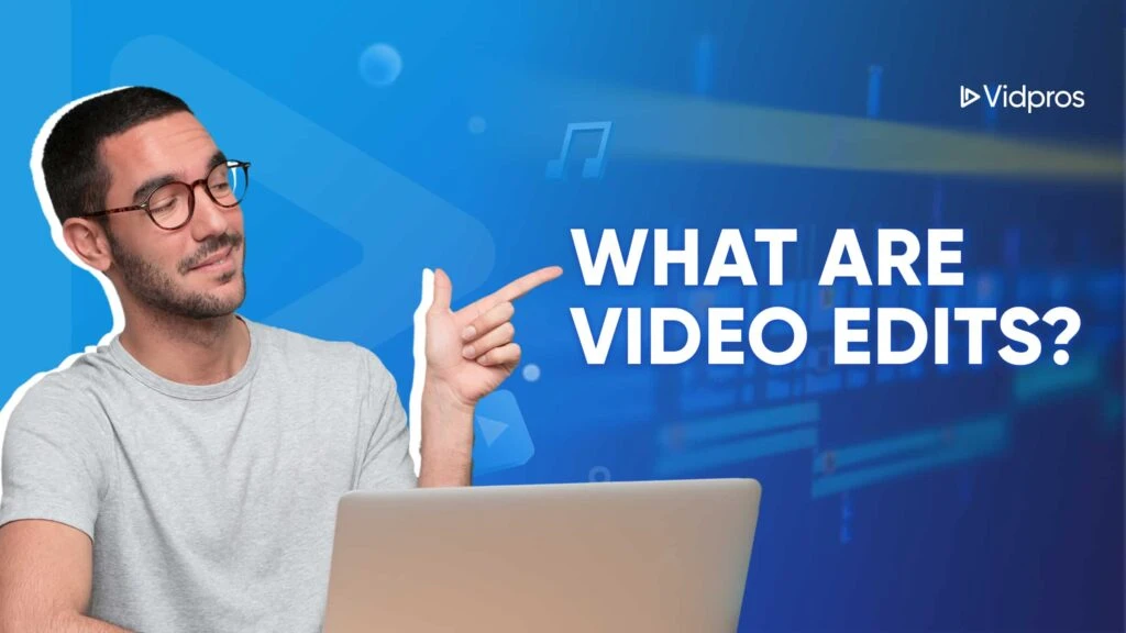 Man with glasses in a gray shirt pointing to the text WHAT ARE VIDEO EDITS? on a blue background adorned with musical icons, highlighting the essence of video edits. A laptop sits before him, capturing his focus. The Vidpros logo is prominently displayed in the top right corner.